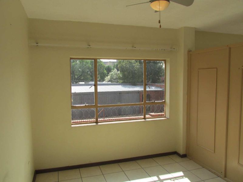 A vacant bedroom featuring tiled flooring, built-in cupboards, and a ceiling fan, offering a blank canvas for potential updates.