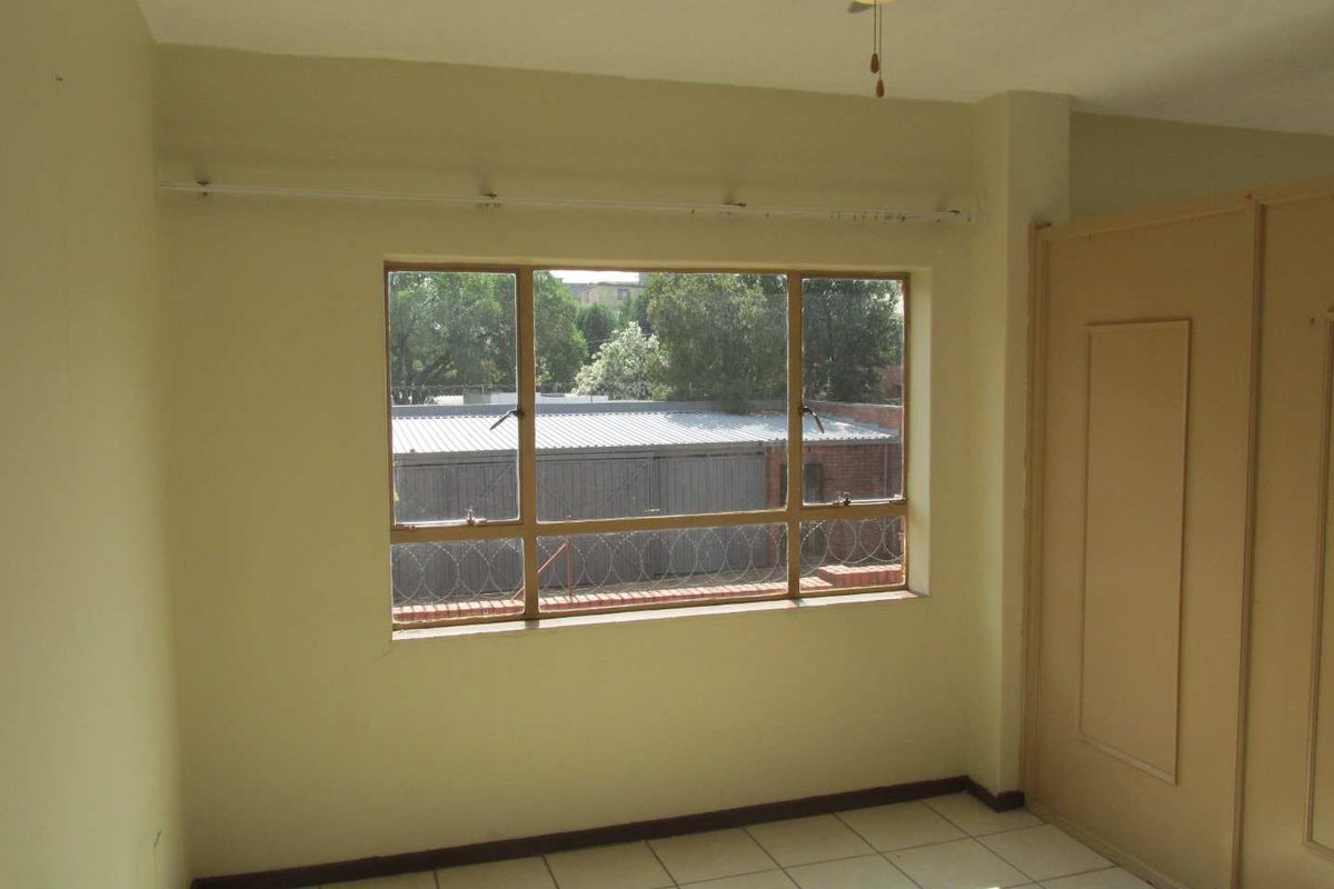 A vacant bedroom featuring tiled flooring, built-in cupboards, and a ceiling fan, offering a blank canvas for potential updates.