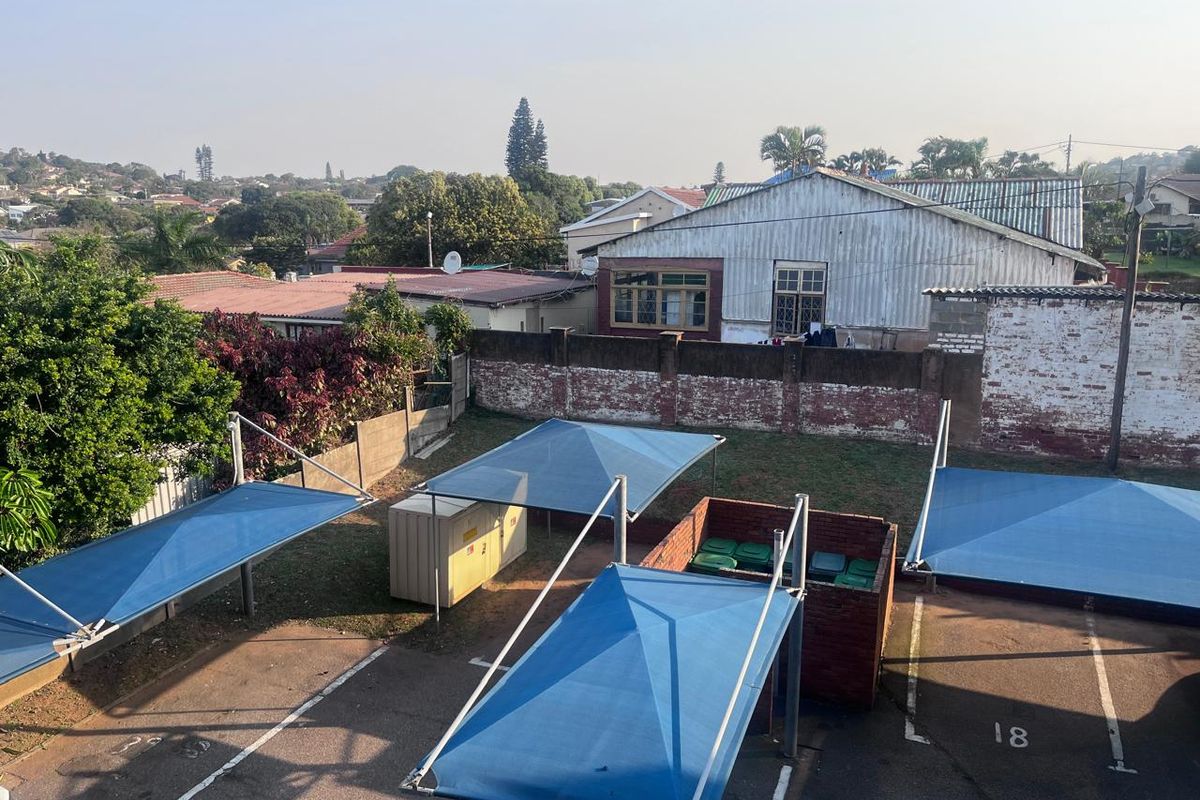 Elevated view of the rear parking area featuring multiple shade cloth carports, a brick refuse enclosure, and perimeter boundary walls.