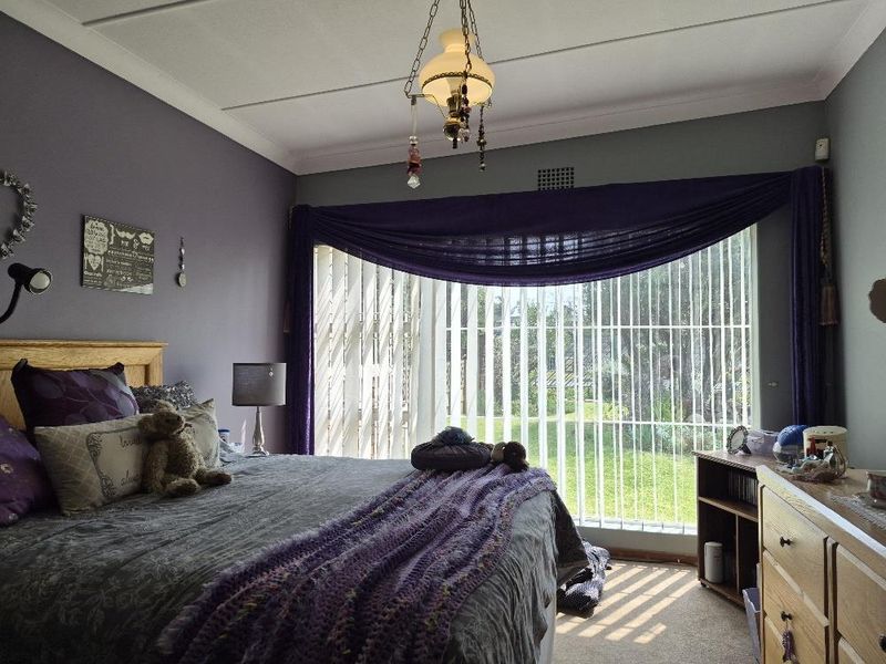 A bedroom featuring large windows with vertical blinds, coving, and a ceiling light fixture, offering natural light and garden views.