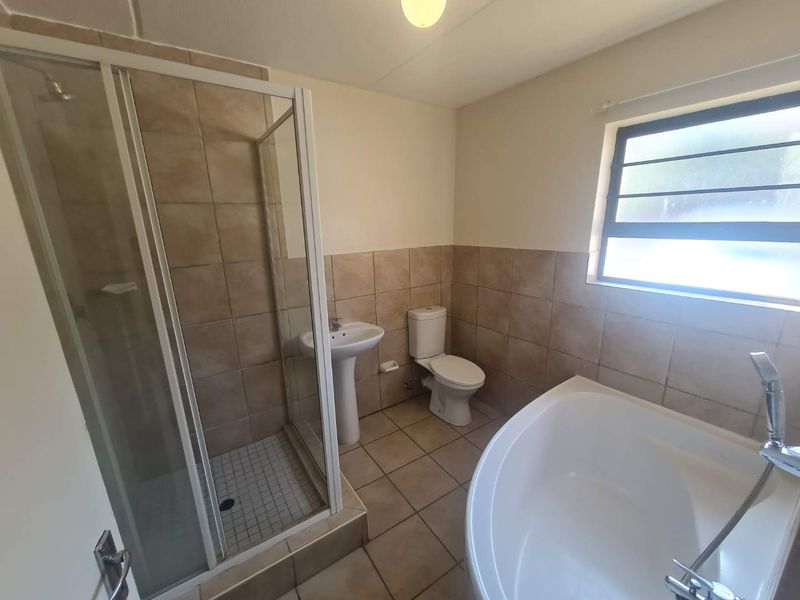 A functional bathroom featuring a separate shower enclosure, bathtub, pedestal basin, and toilet with neutral wall and floor tiling.