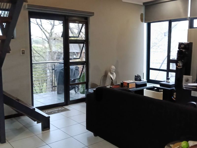 Open-plan living area featuring a modern staircase, tiled flooring, and large windows providing natural light and access to a balcony.