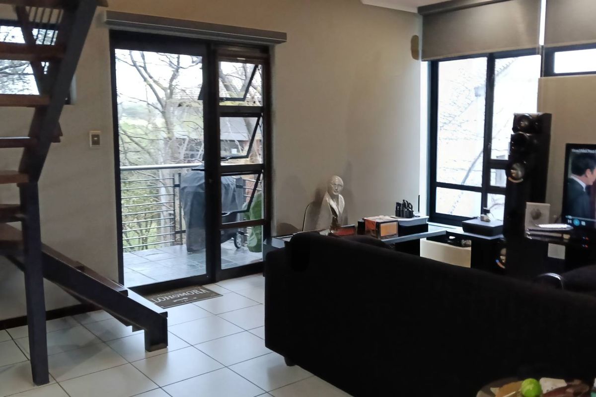 Open-plan living area featuring a modern staircase, tiled flooring, and large windows providing natural light and access to a balcony.