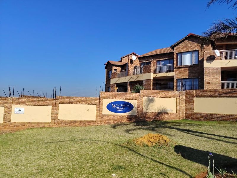 Front exterior view of Winchester Peaks townhouse complex featuring face-brick architecture, perimeter security fencing, and private balconies.