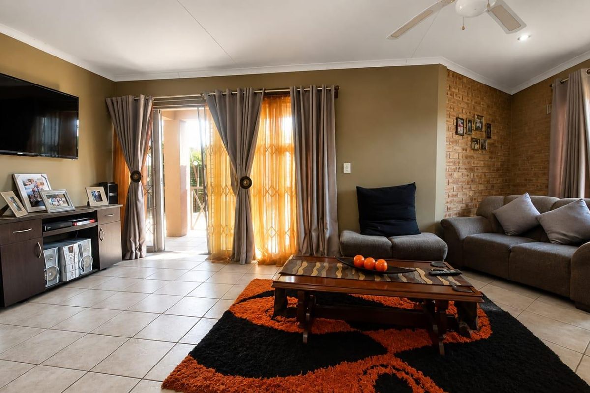 A comfortable living room featuring tiled flooring, an exposed brick accent wall, and a sliding glass door providing access to the outdoor area.