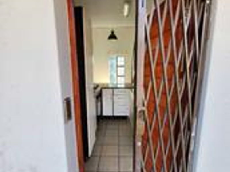 Entrance view into the apartment featuring a security gate, tiled flooring, and a clear line of sight into the kitchen area.