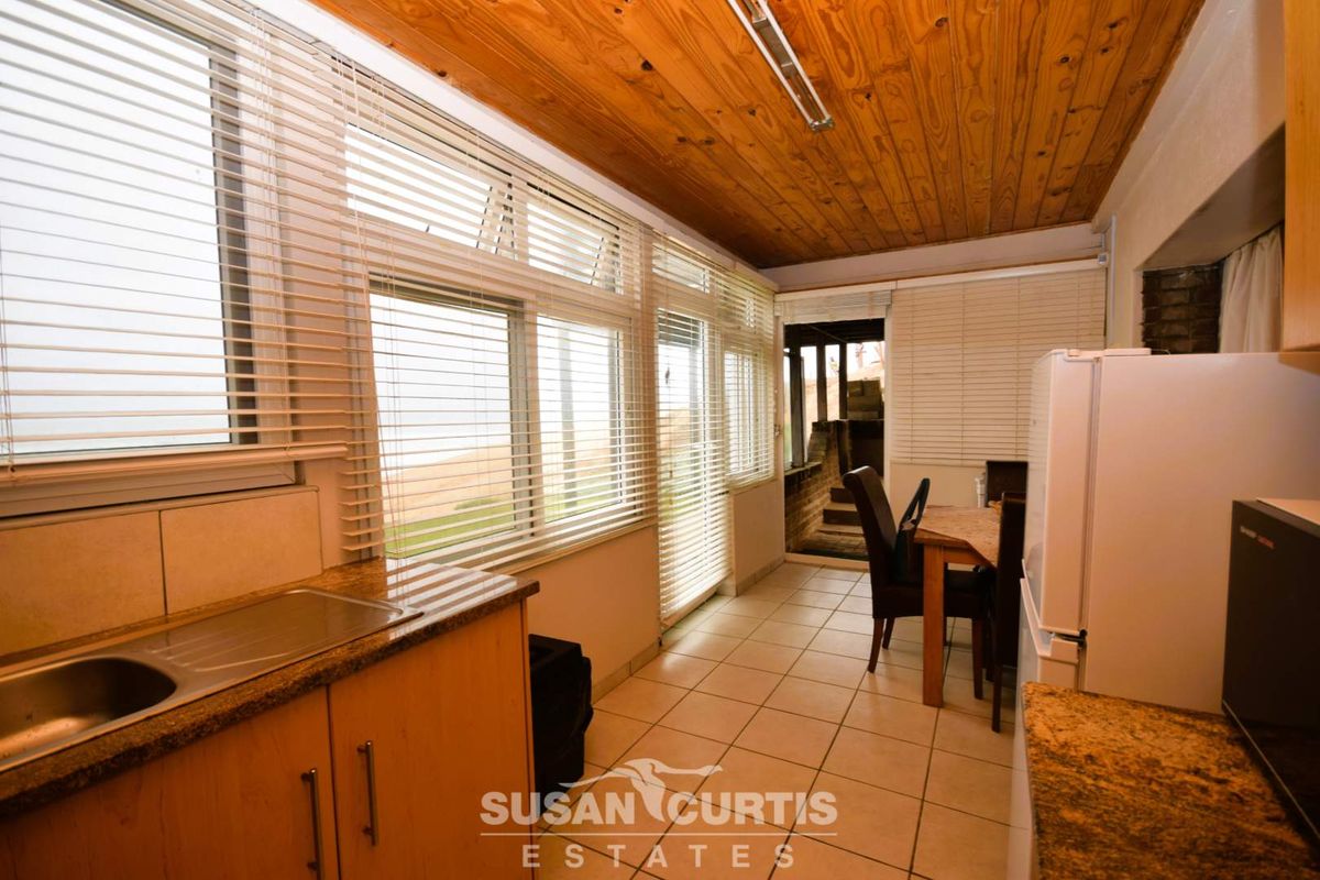 A sun-drenched kitchen area featuring wooden ceiling paneling, tiled flooring, and large windows with blinds, offering a bright and functional space.