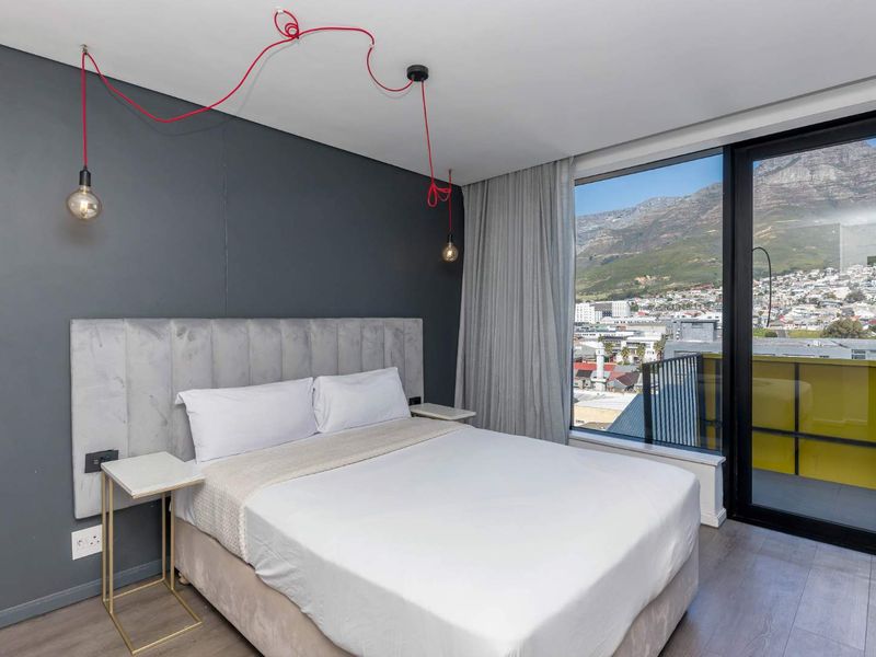 Modern bedroom featuring laminate flooring, a feature wall, and a sliding glass door providing access to a balcony with mountain and city views.