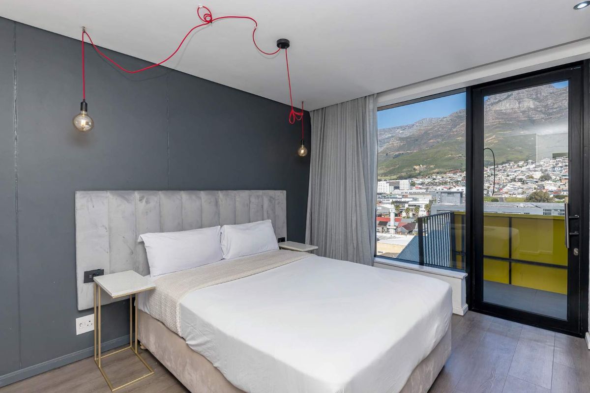 Modern bedroom featuring laminate flooring, a feature wall, and a sliding glass door providing access to a balcony with mountain and city views.