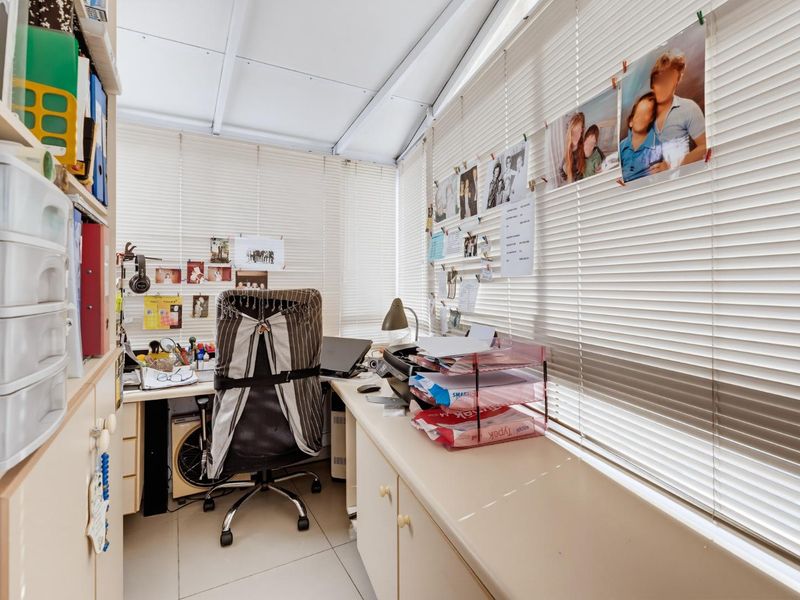 A functional home office space featuring built-in cabinetry, tiled flooring, and large windows with venetian blinds, offering a bright and practical workspace.