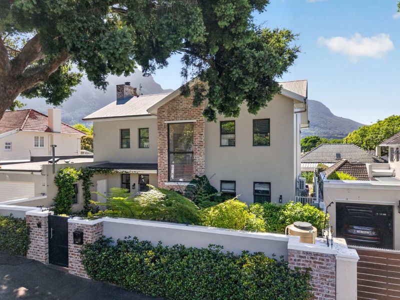 A well-maintained double-story residential property featuring a brick-accented facade, pitched roof, and secure gated entrance with established garden landscaping.