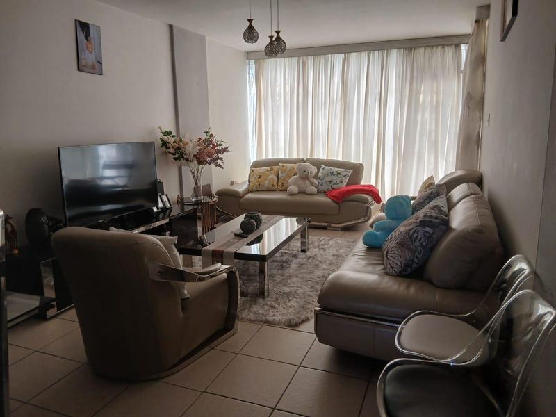 A comfortable living room featuring tiled flooring and large windows, providing a bright and functional space for relaxation.