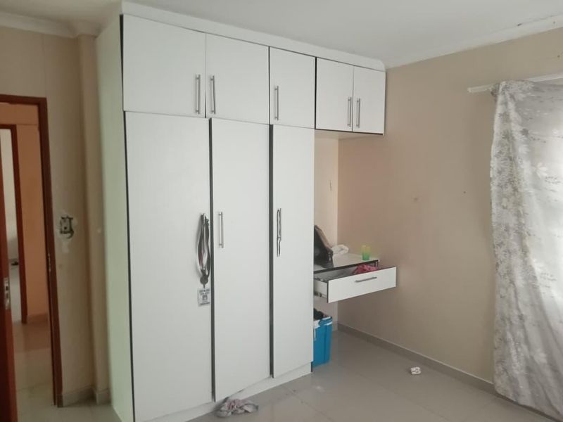 A bedroom featuring white built-in cupboards with overhead storage and an integrated desk unit, providing functional storage and workspace.