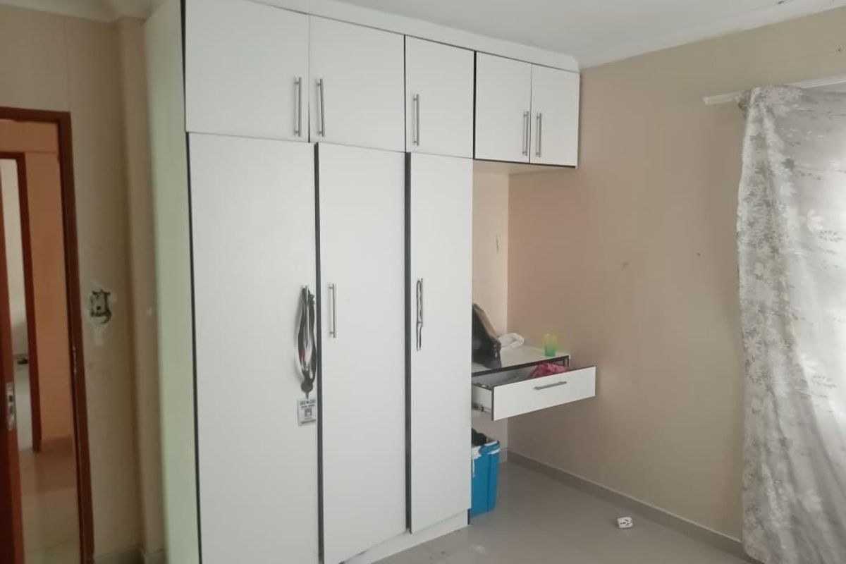 A bedroom featuring white built-in cupboards with overhead storage and an integrated desk unit, providing functional storage and workspace.