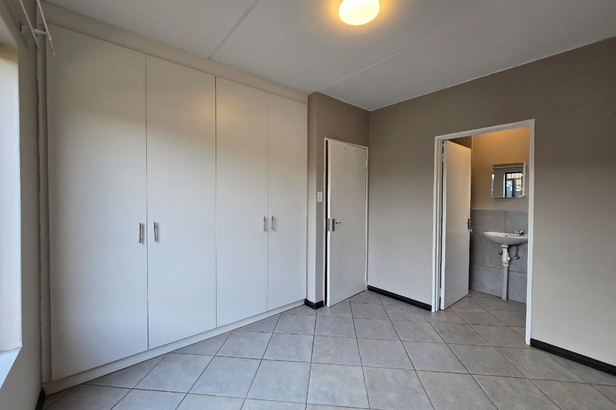 A clean, empty bedroom featuring built-in cupboards, tiled flooring, and an attached en-suite bathroom with a pedestal basin.