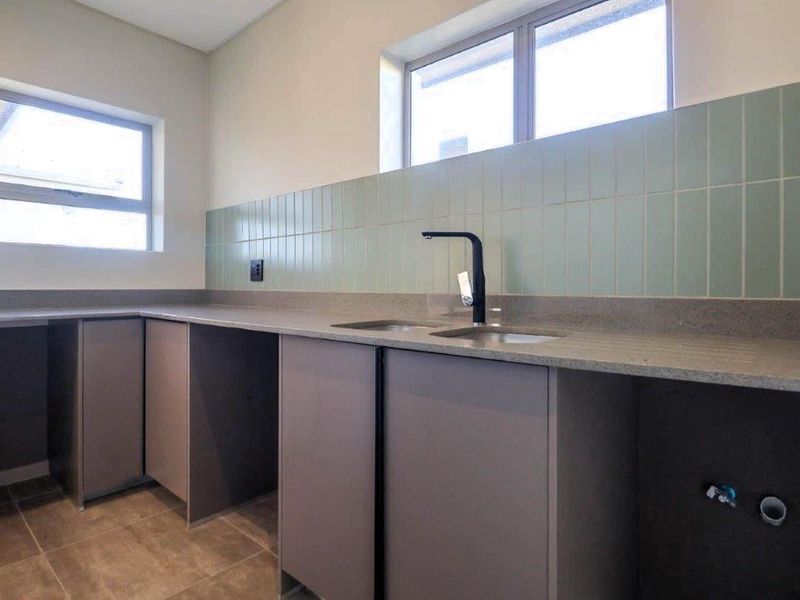 A clean, modern laundry room featuring built-in cabinetry, stone countertops, a double sink with a contemporary mixer tap, and stylish tiled splashbacks.