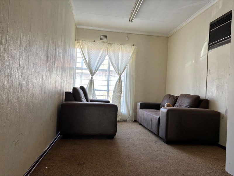A living room featuring a window with security bars, a wall-mounted air conditioning unit, and carpeted flooring.