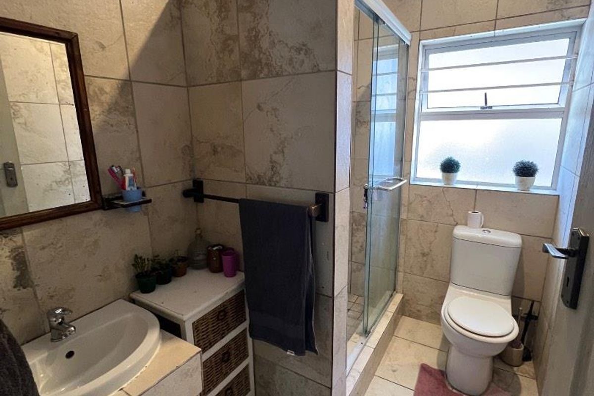 A compact bathroom featuring a tiled shower enclosure, a pedestal-style vanity, and a standard toilet with natural light from a frosted window.