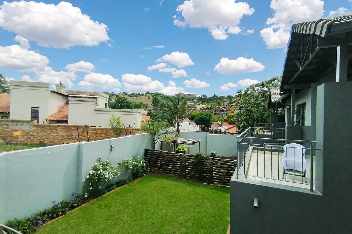 A view of the rear garden featuring a well-maintained lawn, perimeter wall with electric fencing, and an elevated balcony with metal railings.