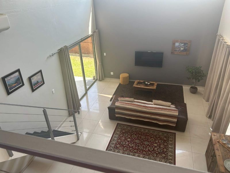 Spacious double-volume living area featuring large format floor tiles, a modern staircase with metal balustrades, and direct access to the garden via sliding doors.