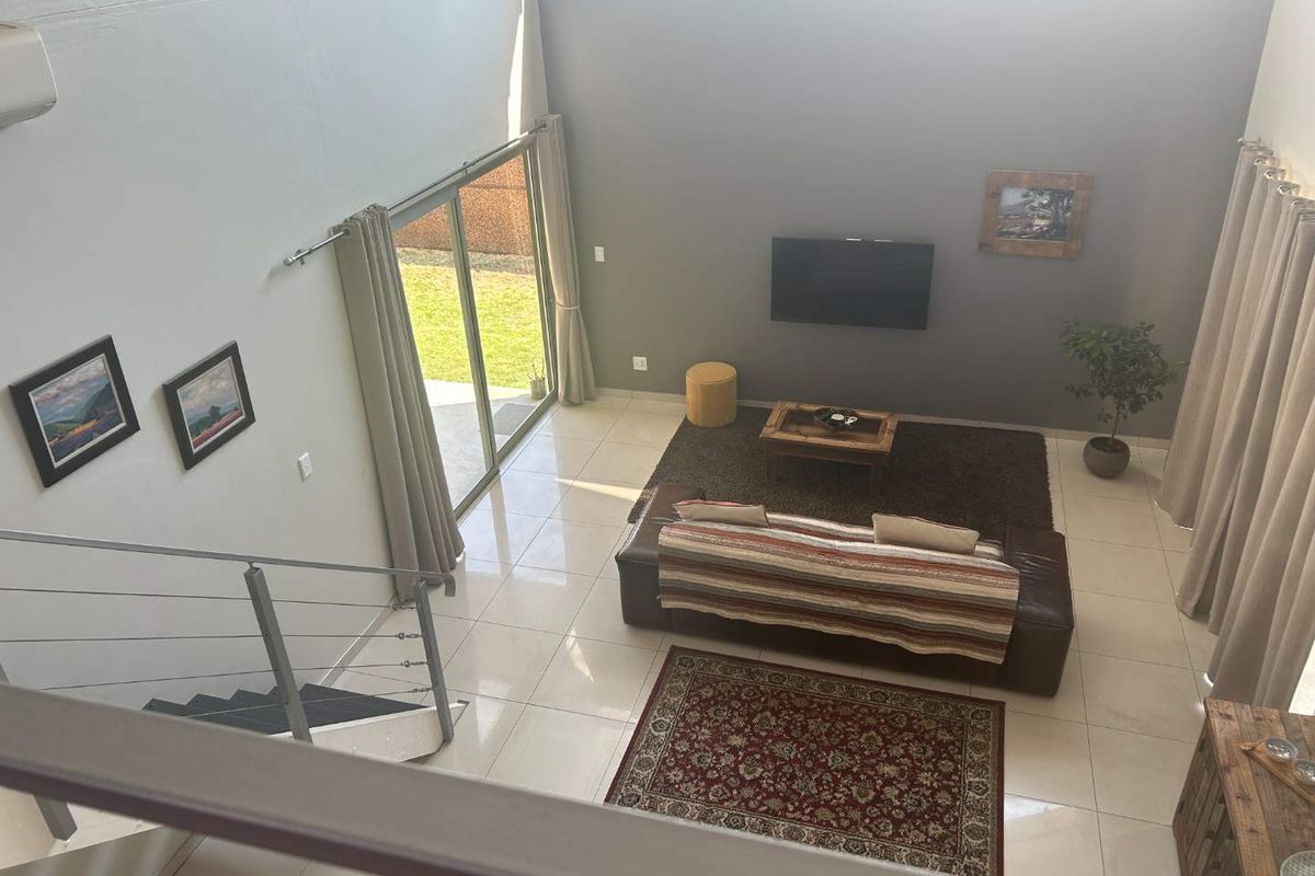 Spacious double-volume living area featuring large format floor tiles, a modern staircase with metal balustrades, and direct access to the garden via sliding doors.