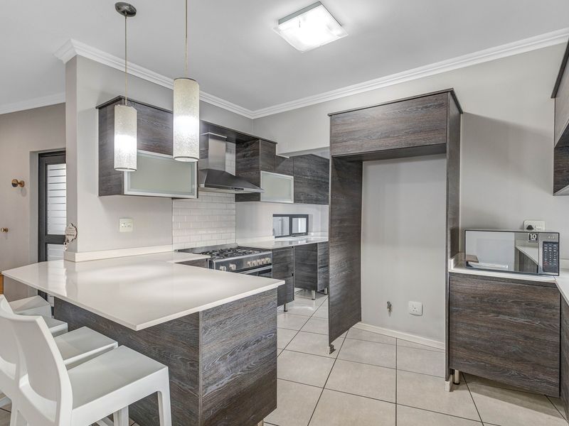 Modern kitchen featuring dark wood-grain cabinetry, stone countertops, a gas hob with extractor, and a breakfast bar with pendant lighting.