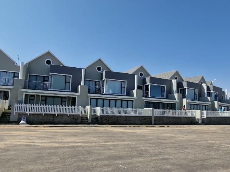 A row of modern townhouses featuring pitched roofs, private balconies, and white picket fencing, set against a clear sky.