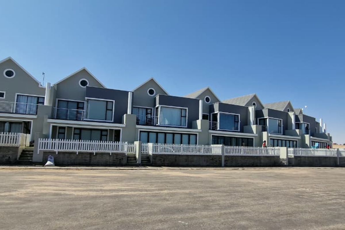 A row of modern townhouses featuring pitched roofs, private balconies, and white picket fencing, set against a clear sky.