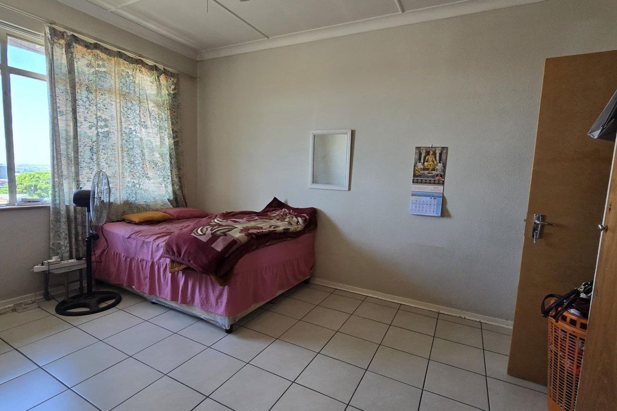 A bedroom featuring tiled flooring, a large window with natural light, and a standard wooden door.
