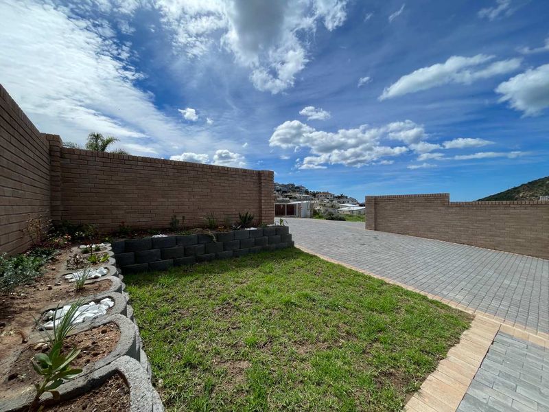A well-maintained front exterior featuring a paved driveway, brick boundary walls, and a landscaped garden area with a retaining wall.