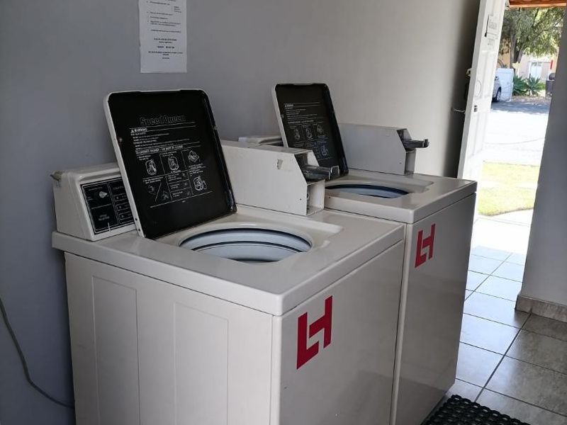 A functional communal laundry area featuring two commercial washing machines and tiled flooring with direct access to the exterior.