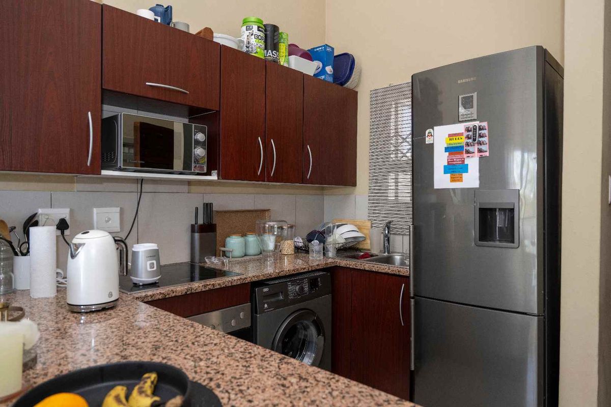 Compact kitchen featuring dark wood cabinetry, granite countertops, integrated sink, and space for a washing machine.