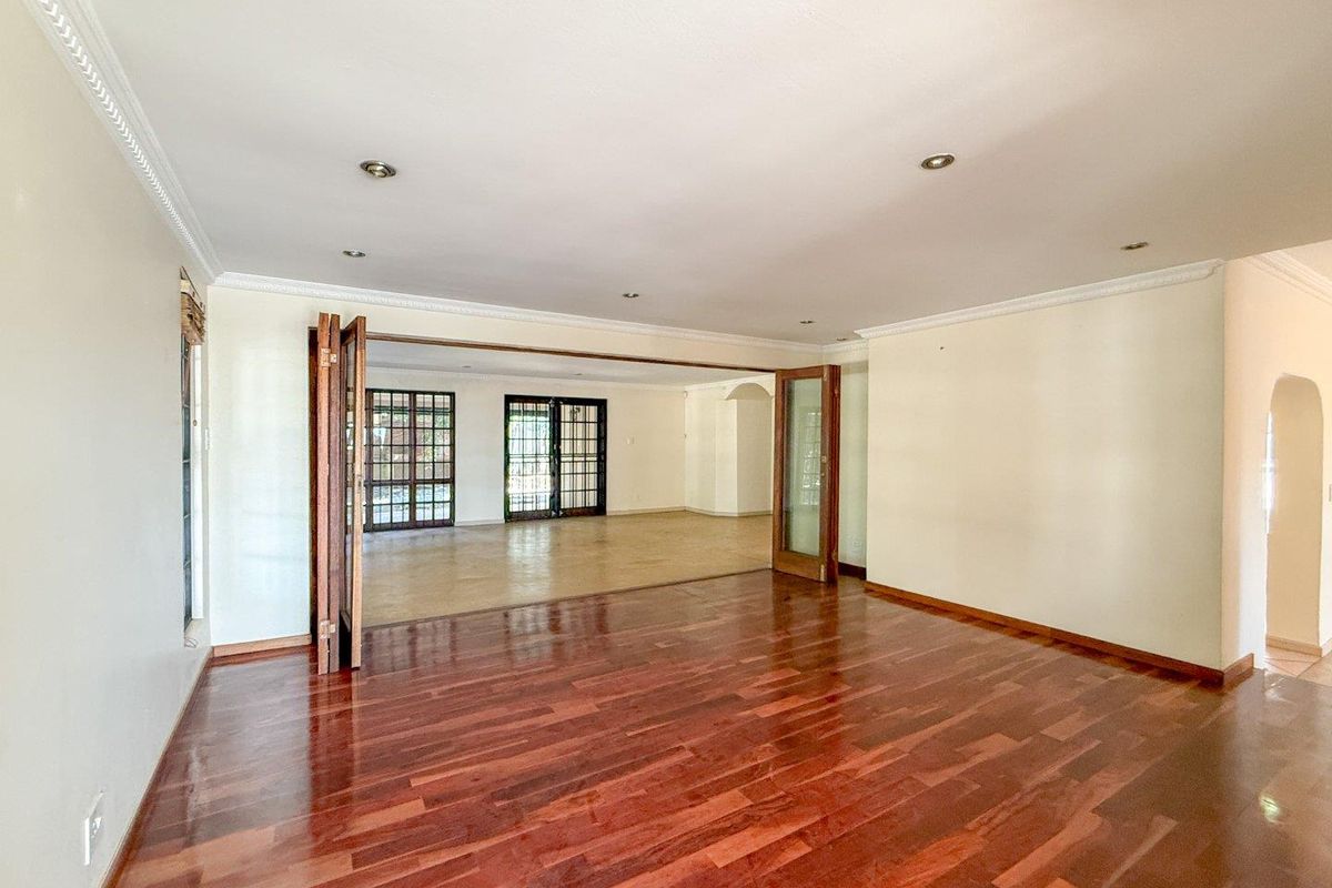 Spacious living area featuring polished hardwood flooring, recessed downlighting, decorative crown molding, and large wooden folding doors connecting to an adjacent room.