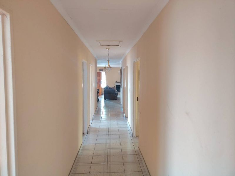 A long, neutral-toned hallway featuring tiled flooring and a central ceiling light, providing access to multiple rooms within the home.