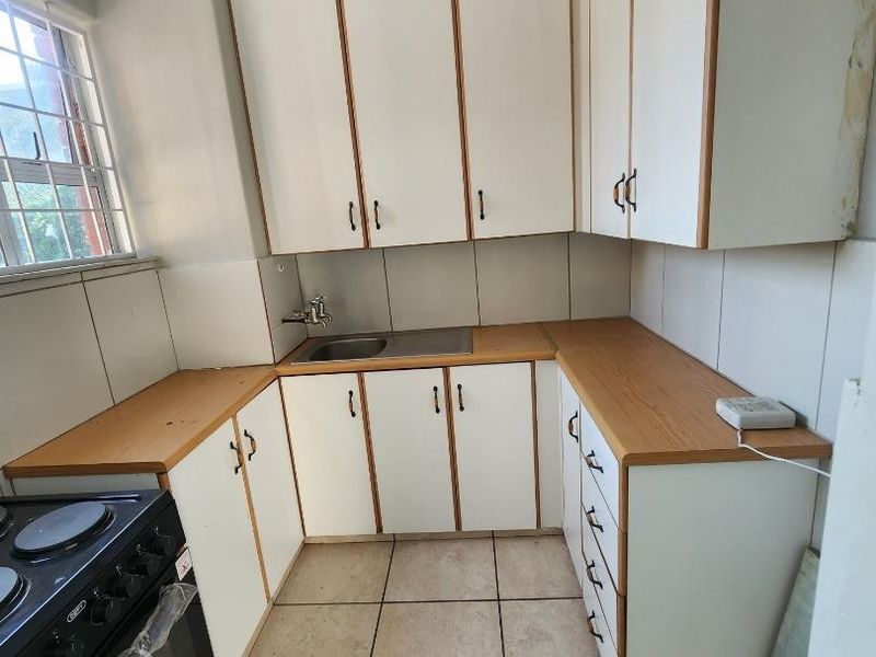 A compact kitchen featuring laminate countertops, white cabinetry, and ceramic floor tiles, offering a functional layout with potential for modern cosmetic updates.