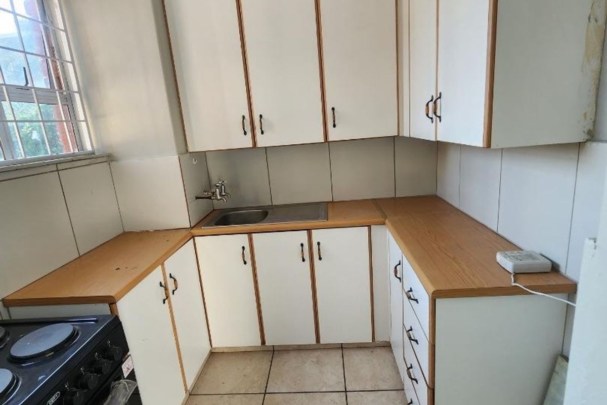A compact kitchen featuring laminate countertops, white cabinetry, and ceramic floor tiles, offering a functional layout with potential for modern cosmetic updates.