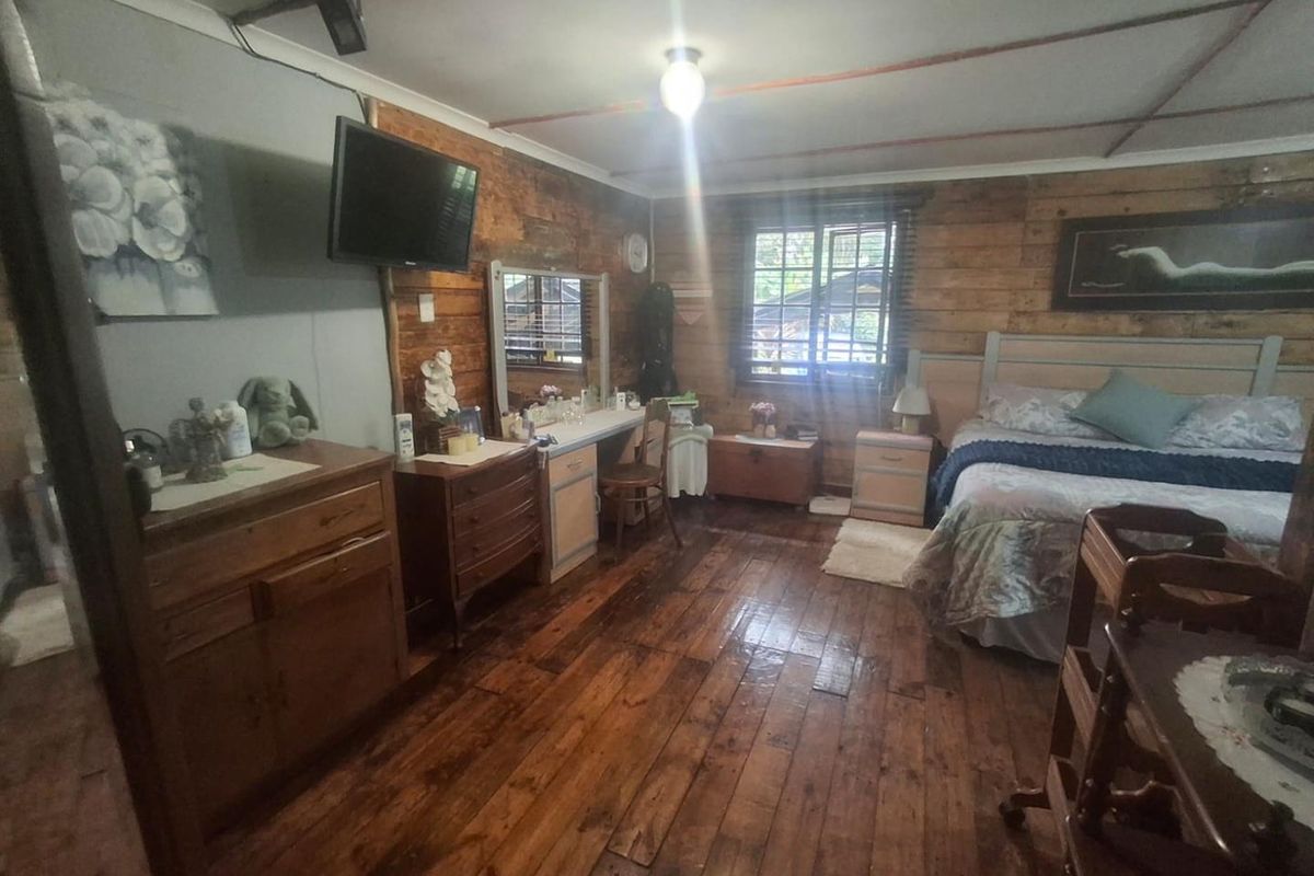 Spacious bedroom featuring rustic timber wall cladding and hardwood flooring, offering a warm cottage aesthetic with potential for modern updates.