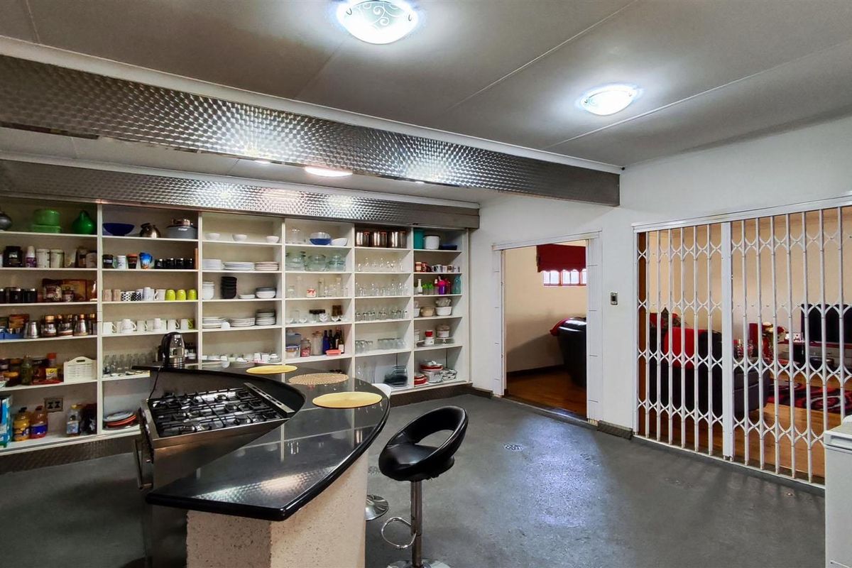 A spacious kitchen featuring extensive built-in shelving, a curved breakfast bar with a gas hob, and a security gate leading to an adjacent room.
