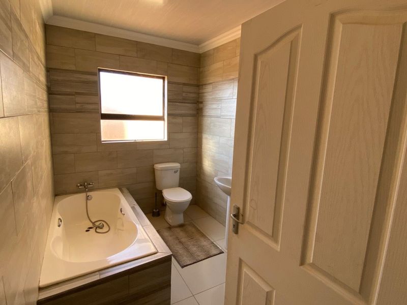 A modern bathroom featuring tiled walls, a built-in bathtub with shower mixer, a pedestal basin, and a toilet.