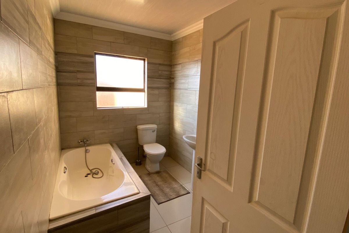 A modern bathroom featuring tiled walls, a built-in bathtub with shower mixer, a pedestal basin, and a toilet.