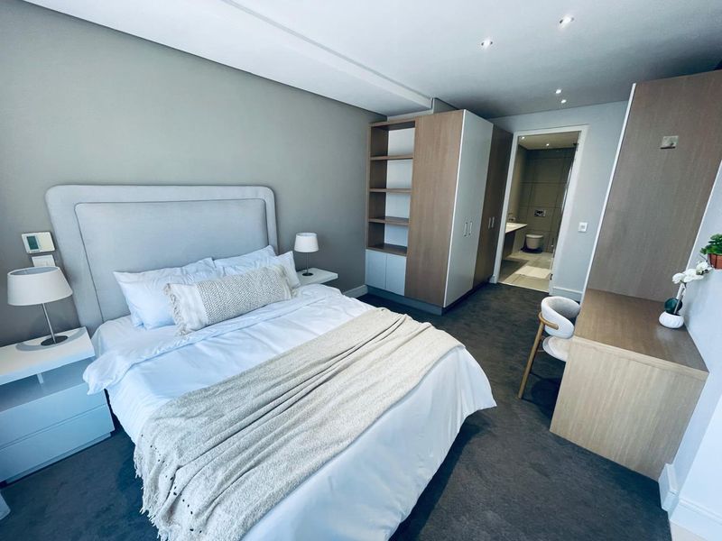 Modern bedroom featuring built-in cabinetry, recessed lighting, plush carpeting, and an adjoining en-suite bathroom.