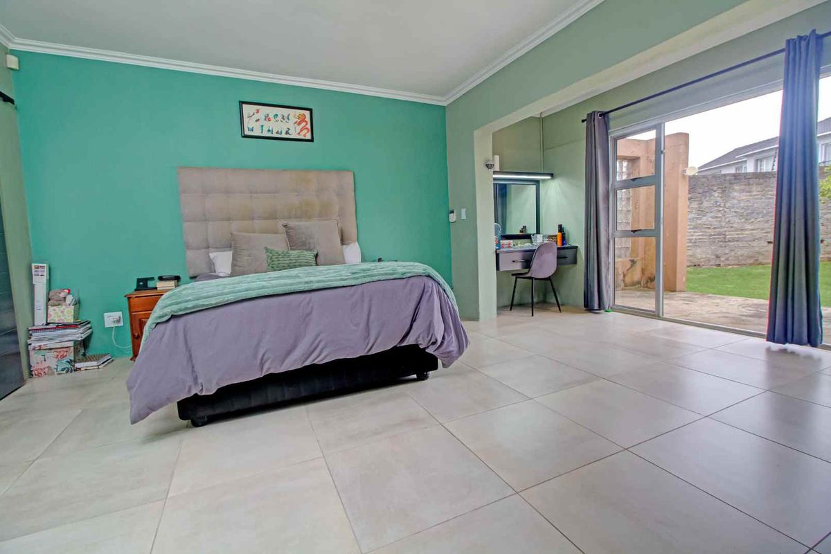 Spacious bedroom featuring large format floor tiles, a feature wall, and sliding glass doors providing direct access to the rear garden.
