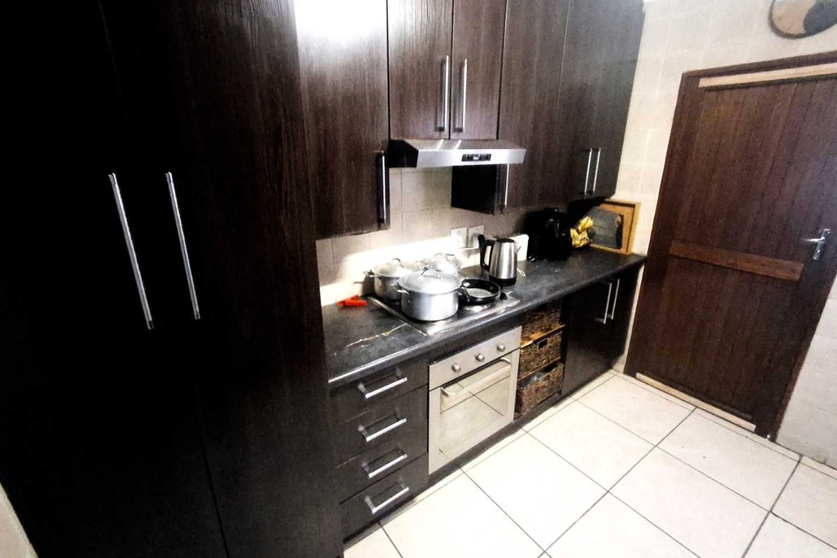 A functional kitchen featuring dark wood cabinetry, built-in oven, extractor fan, and tiled flooring with a neutral backsplash.