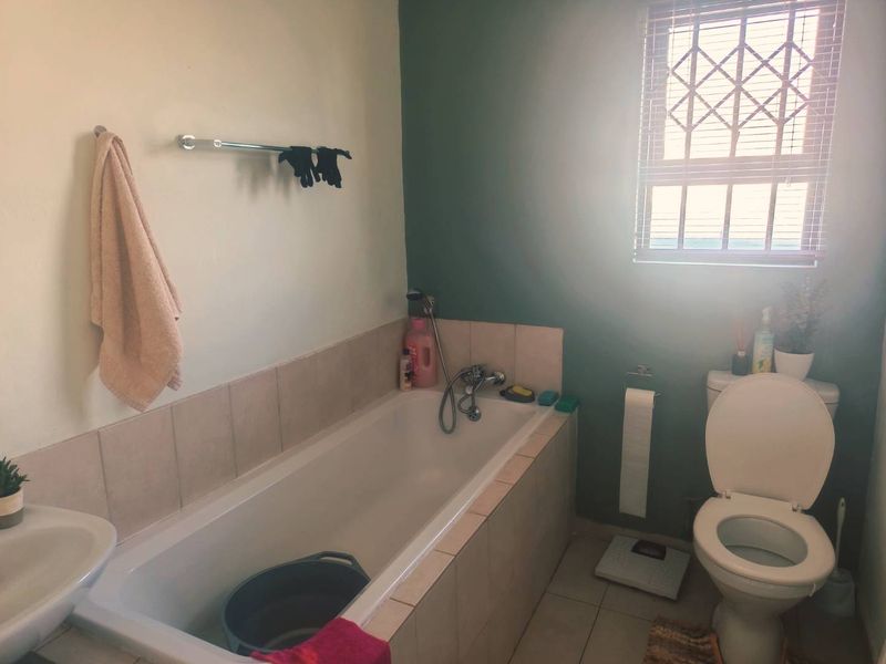 A functional bathroom featuring a built-in bathtub with tiled surround, a pedestal basin, and a toilet, finished with neutral wall tones and tiled flooring.