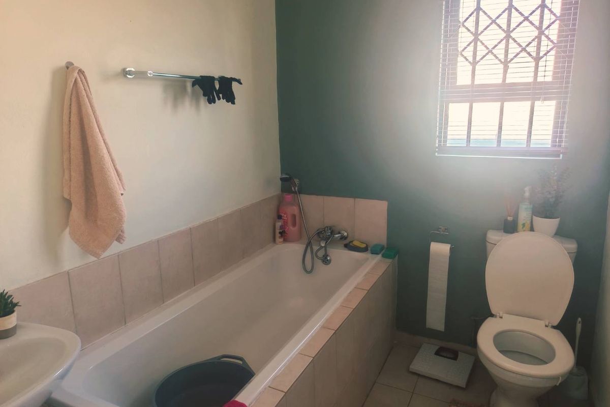 A functional bathroom featuring a built-in bathtub with tiled surround, a pedestal basin, and a toilet, finished with neutral wall tones and tiled flooring.