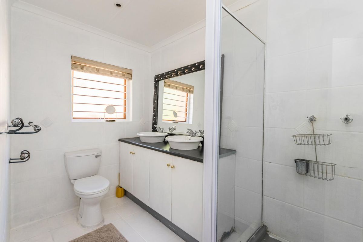 A functional bathroom featuring a double vanity with vessel sinks, a glass-enclosed shower, and a toilet, finished with white wall tiles.