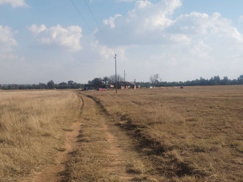 A wide-angle view of a rural farm property featuring a dirt access track leading toward the main dwelling and surrounding open fields.