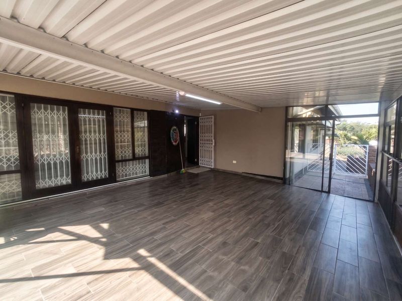 A spacious covered patio featuring modern wood-look floor tiles, secure sliding glass doors, and a corrugated metal roof, ideal for outdoor entertaining.