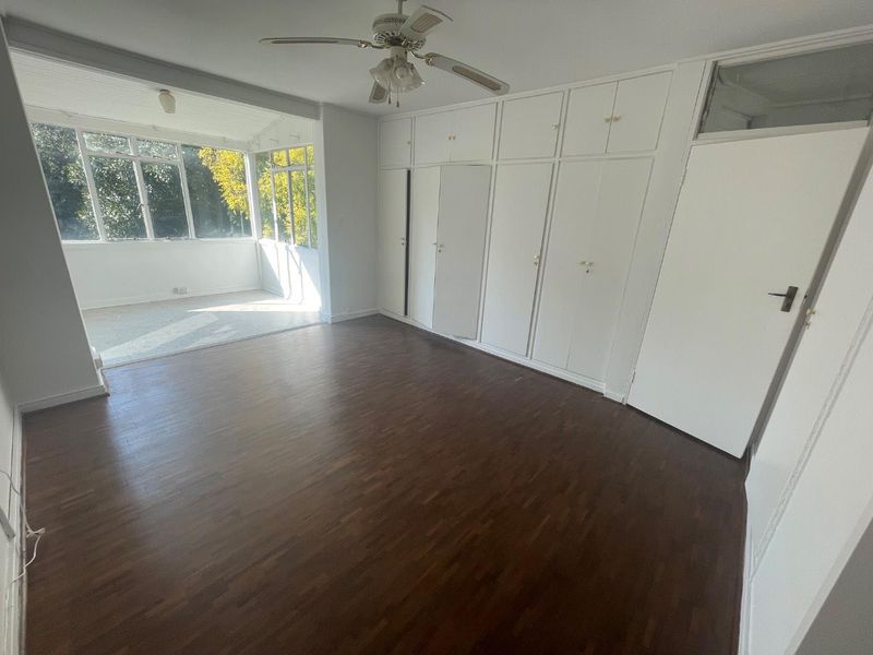 Spacious bedroom featuring classic parquet flooring, extensive built-in cupboard storage, a ceiling fan, and an adjoining sunroom with large windows.