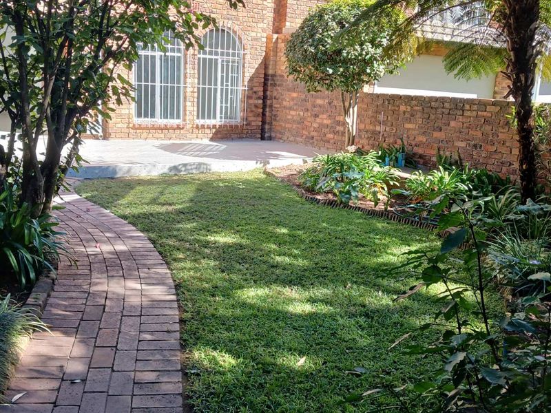 A private rear garden featuring a brick-paved pathway, a small lawn, and a concrete patio area enclosed by brick boundary walls.